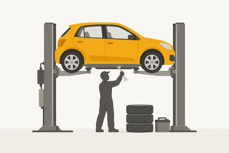 A mechanic working under a yellow car raised on a lift, with tyres and a battery beside him